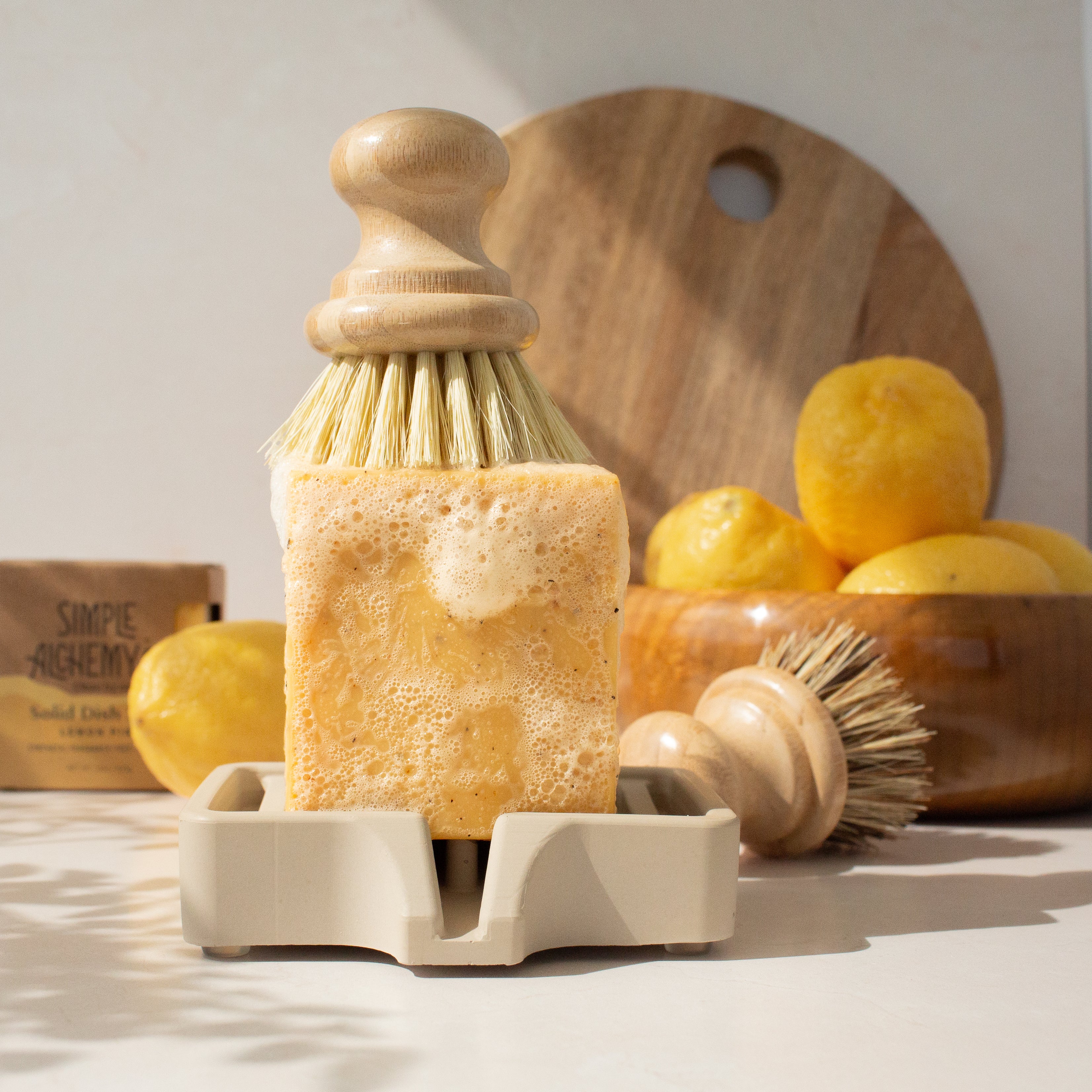 Lemon Pine bar on a self-draining soap dish with dish brushes and kitchen tools