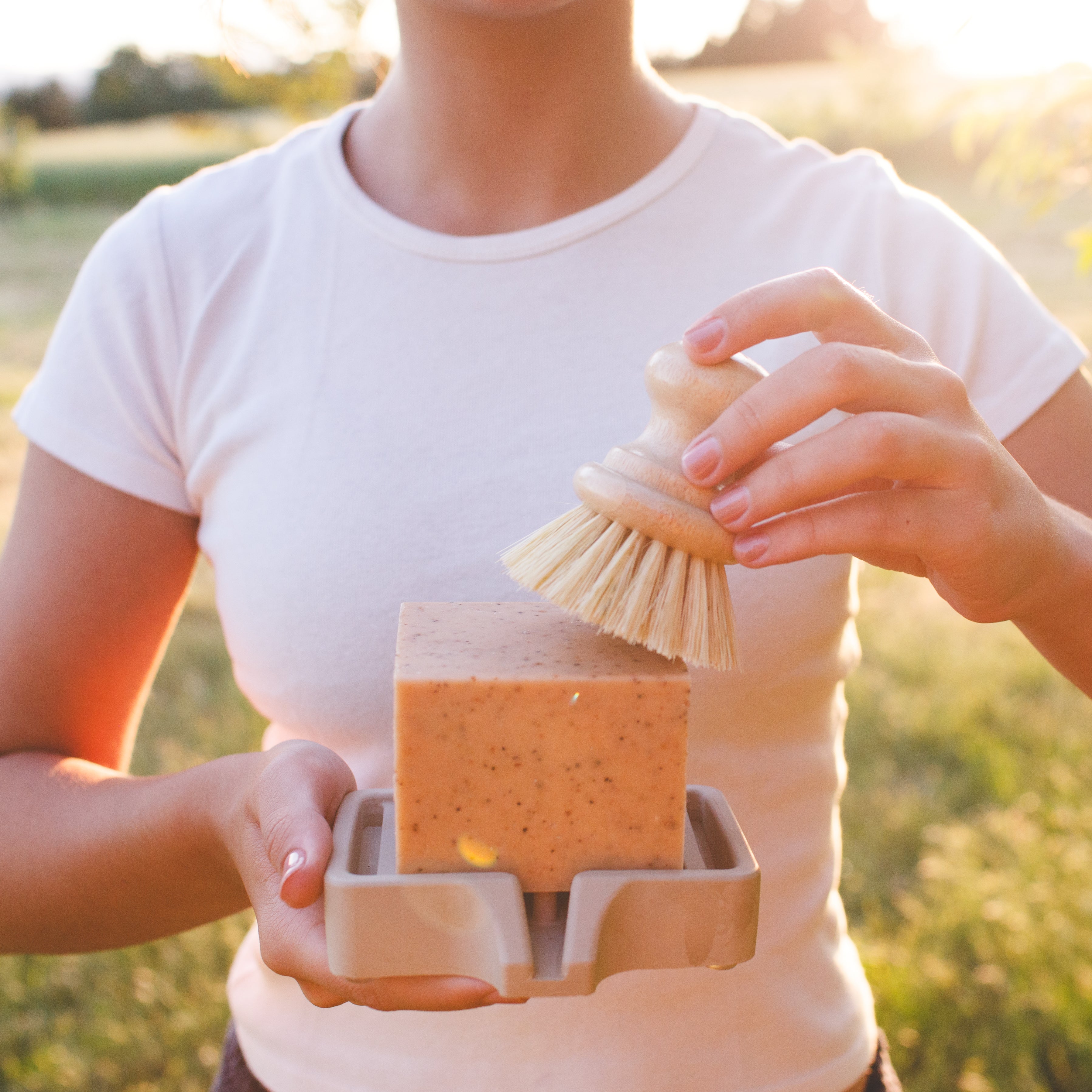 Person using a dish brush with Lemon Pine Solid Dish Soap outdoors in natural light
