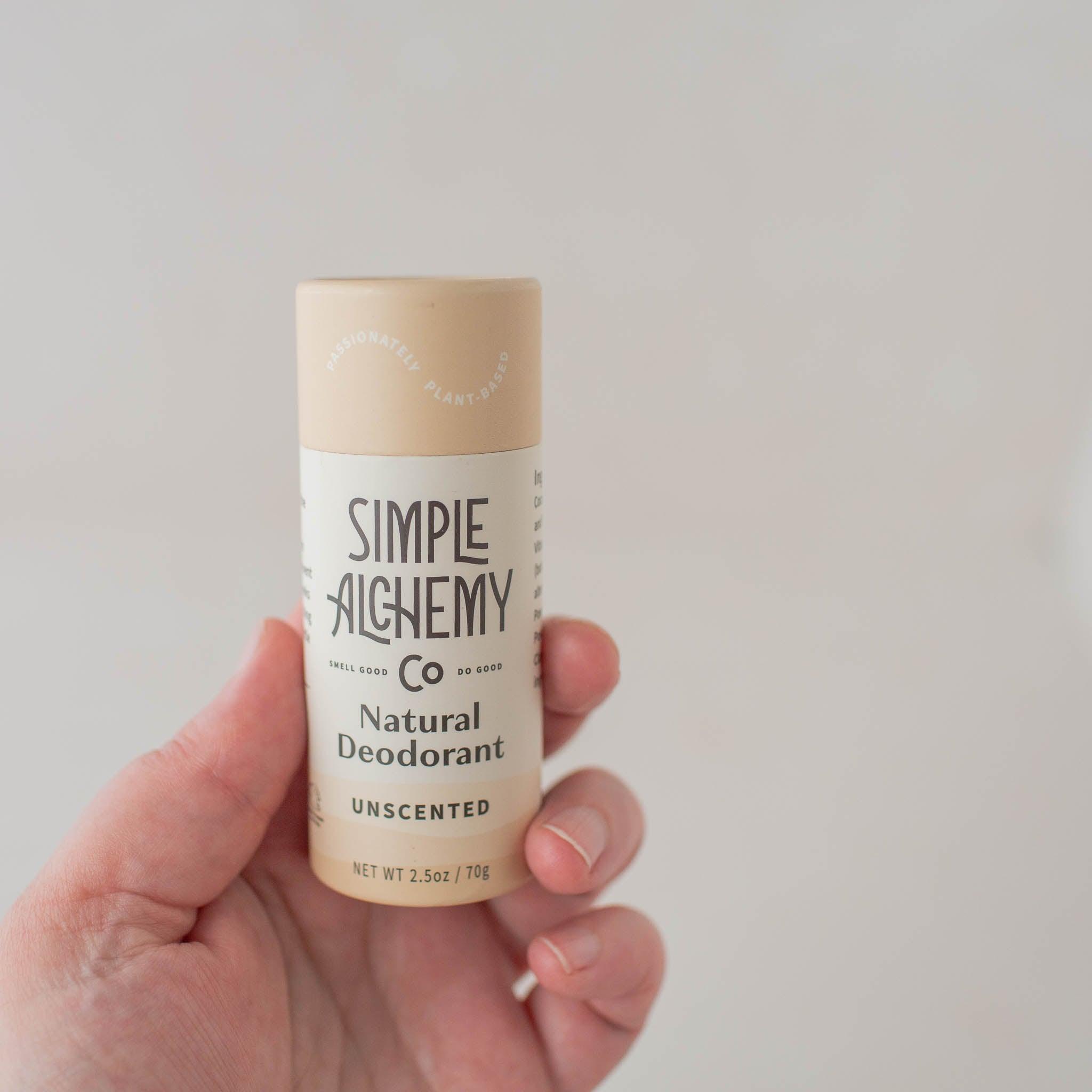 Hand holding cream colored compostable paper push-up tube of Unscented Natural Deodorant.