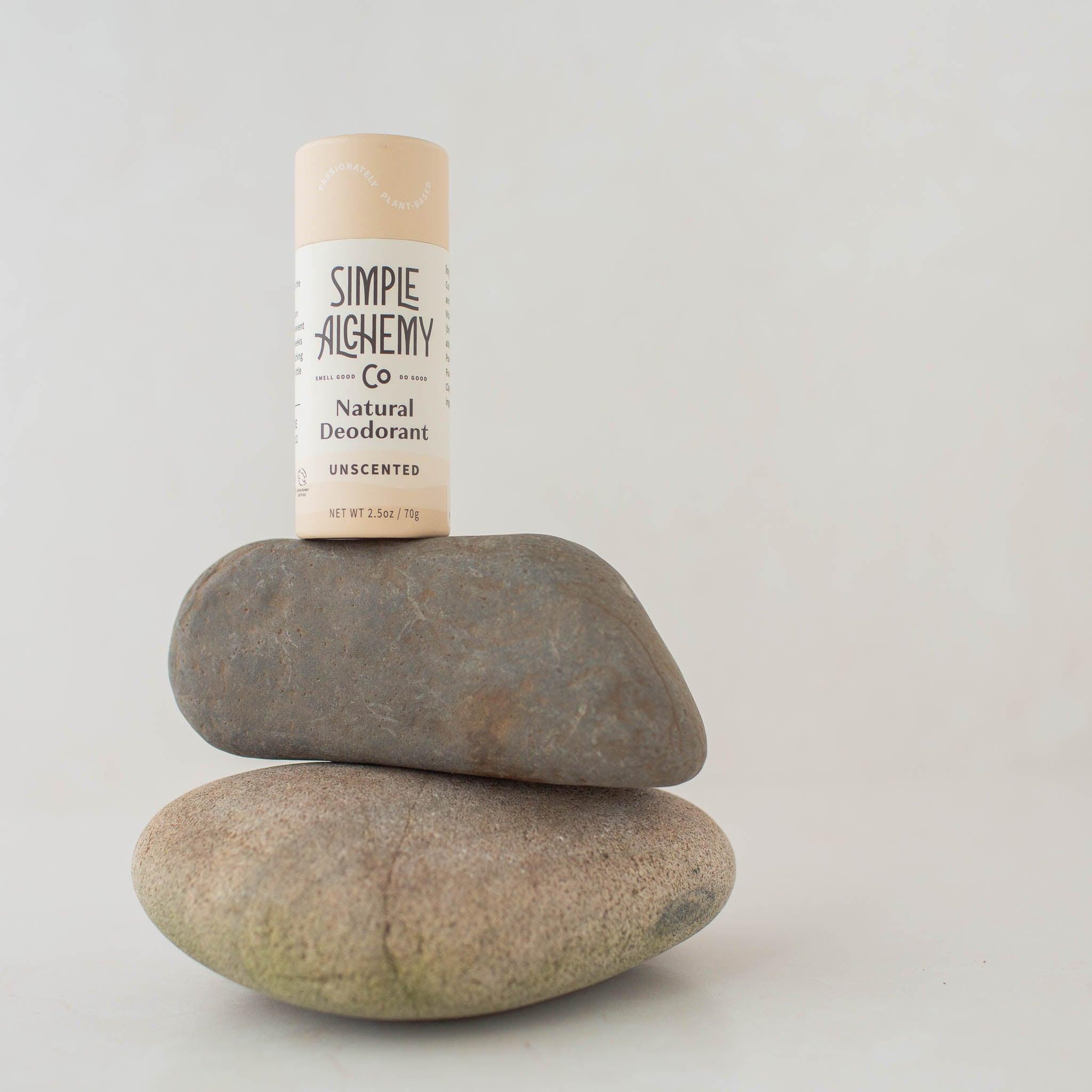 Cream colored compostable paper push-up tube of Unscented Natural Deodorant on two gray stones.