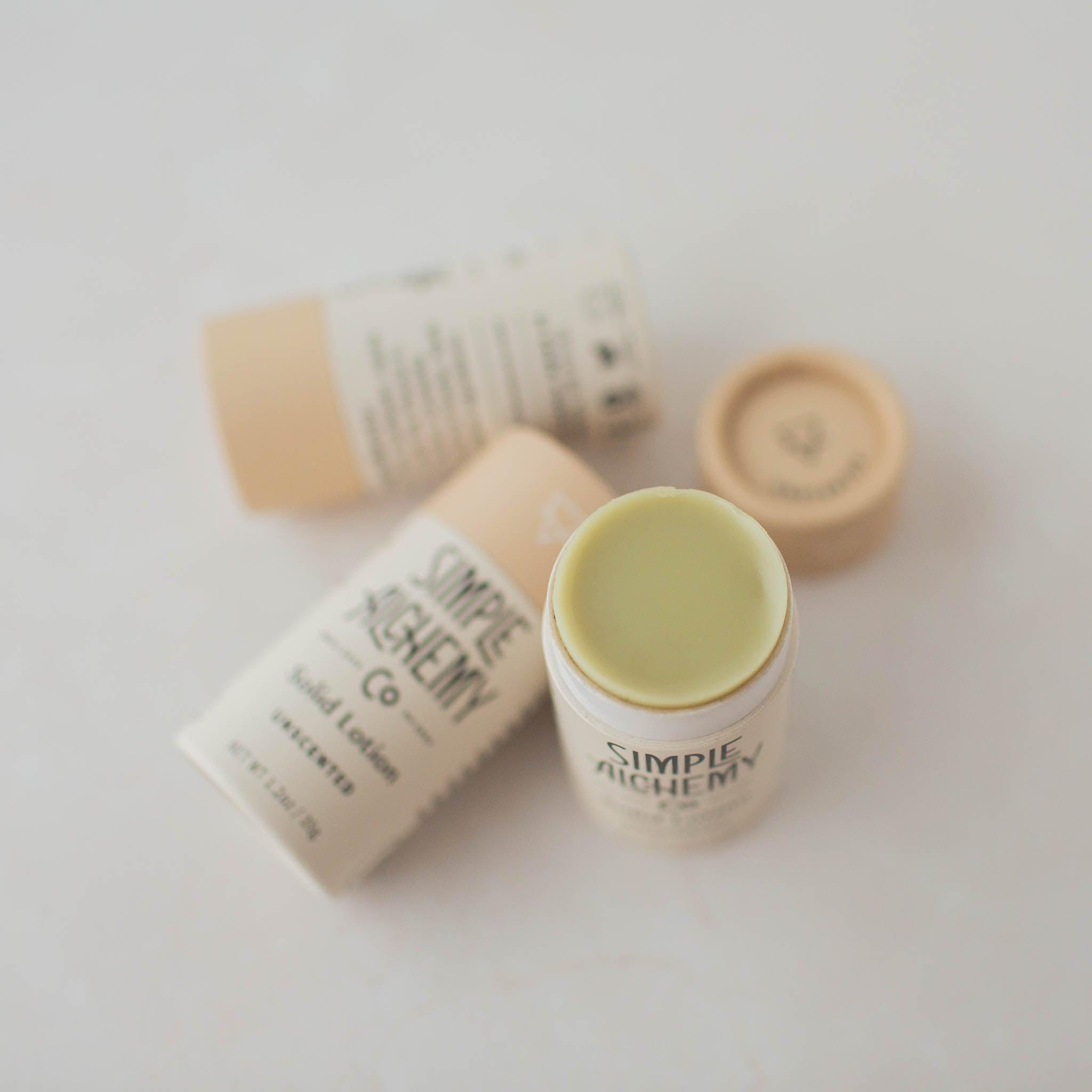 Trio of cream colored compostable tubes of Unscented Solid Lotion, one with cap off showing pale matcha colored lotion.