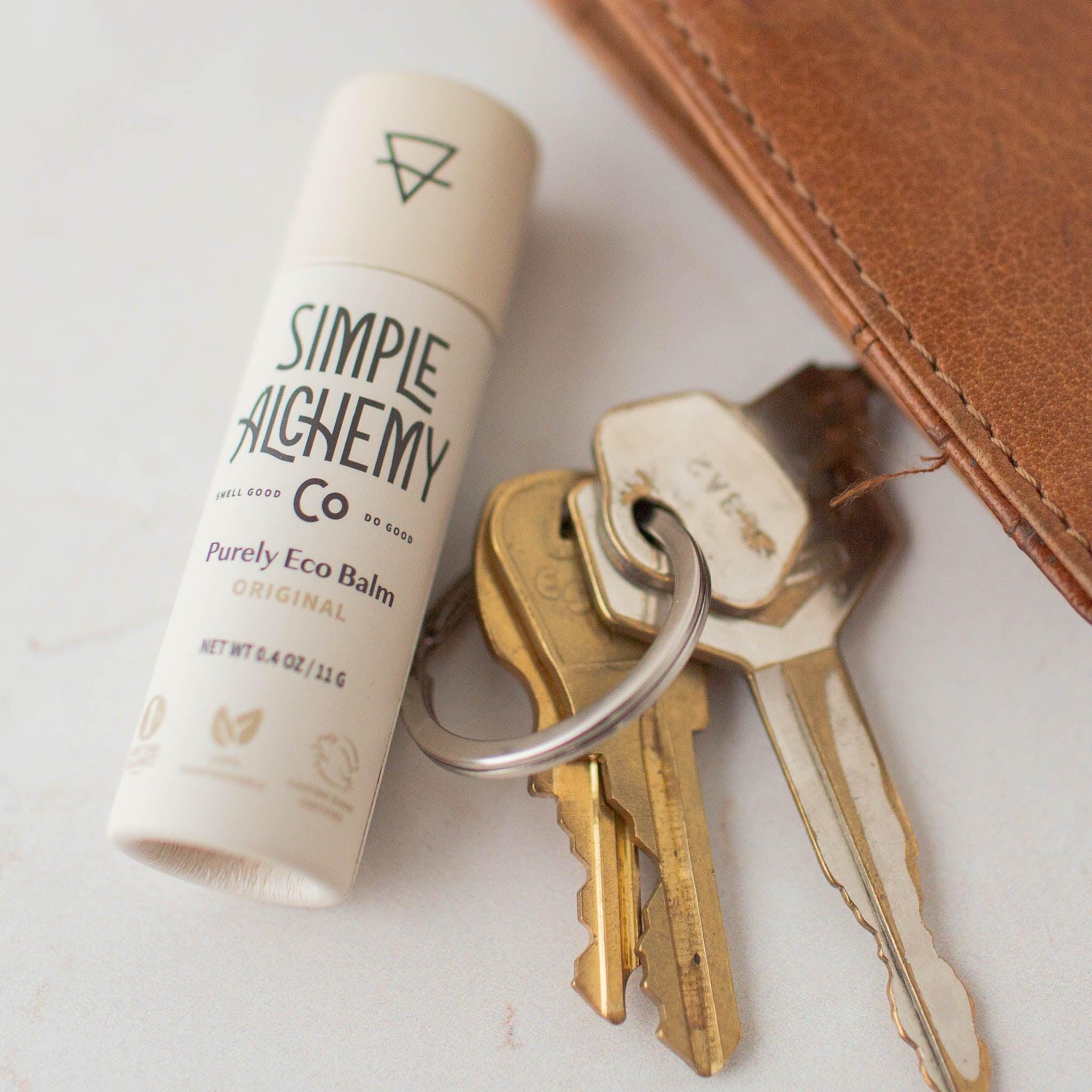 Off-white compostable paper tube of original vegan lip balm with keys and wallet.